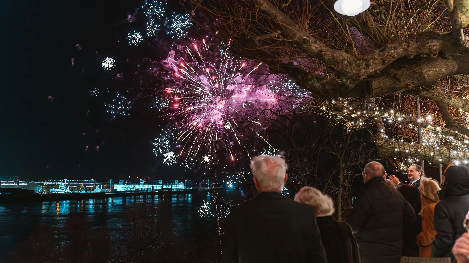 A group of people are watching the New Year’s Eve fireworks from the Linden Terrace at the Louis C. Jacob Hotel in Hamburg.