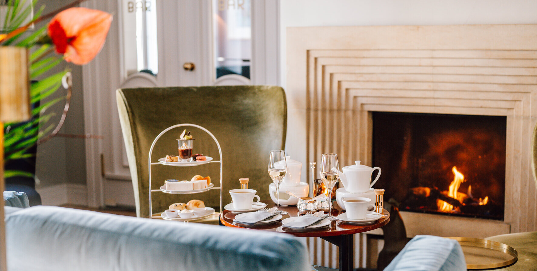 A table with tea service and glasses in front of a fireplace in a living room.