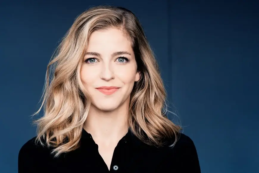 Karina Canellakis Karina Canellakis steht vor einem dunkelblauen Hintergrund und lächelt in die Kamera.