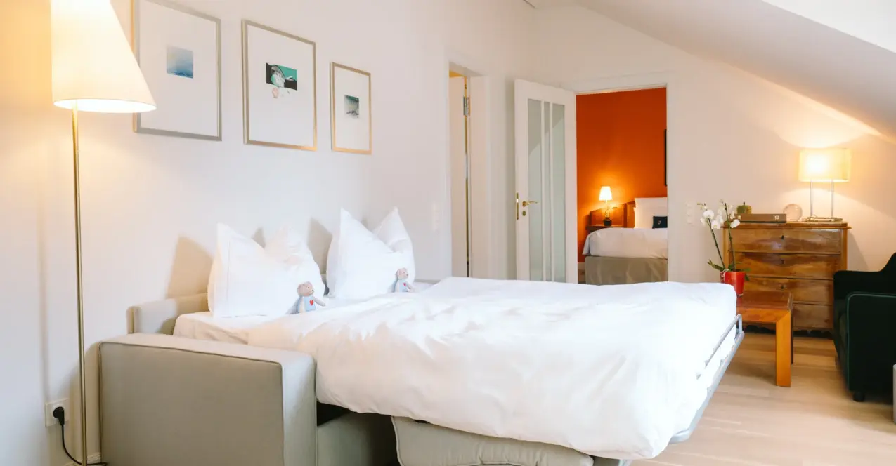 A stylishly furnished hotel room with two sleeping areas, bedside table and decorative lamp.