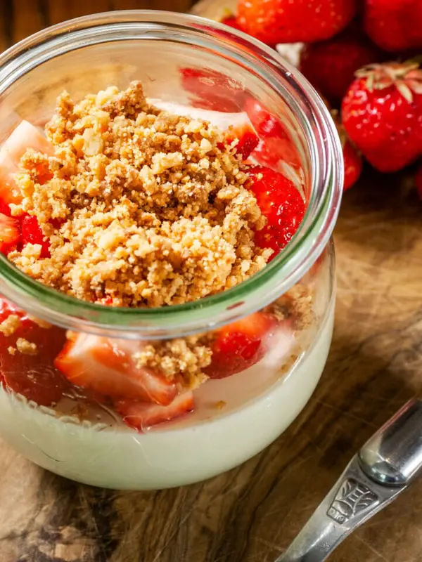 A jar of dessert with strawberries and a spoon.