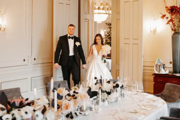A wedding couple are standing next to a laid table indoors